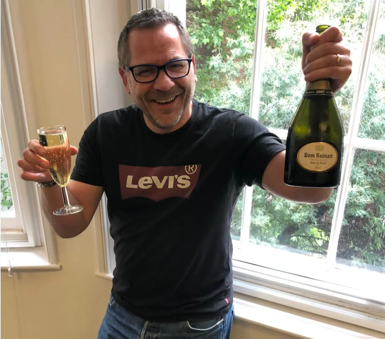 Giuseppe Russo smiling, holding a glass and a bottle of champagne